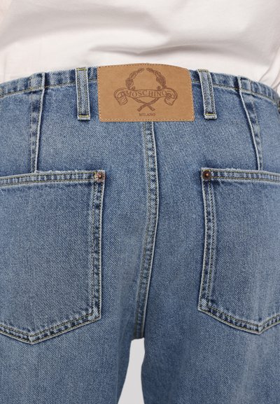 Šviesiai mėlynos džinsinės kelnės su aukštu juosmeniu, turinčios rudą odinį ženklą su užrašu "Moschino Milano" ir dviem gale esančiomis kišenėmis.