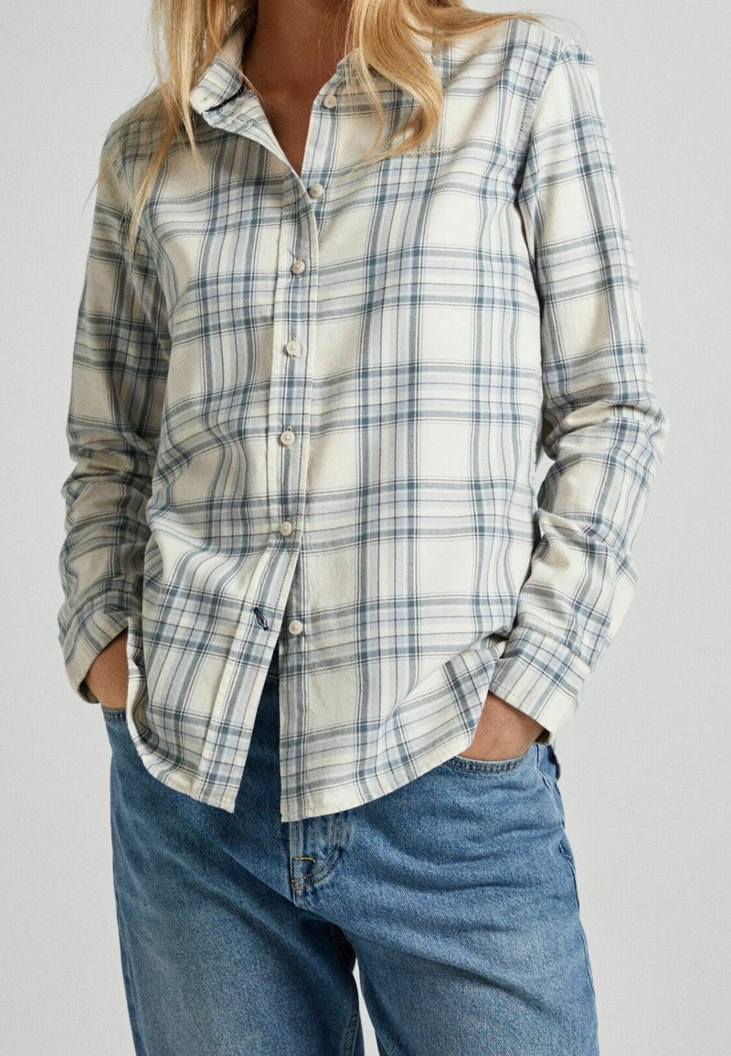 Lys beige button-up skjorte med blå ternet mønster. Lavet af blødt stof, med krave og knappet front, parret med afslappede blå jeans.