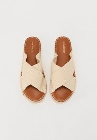Beige krossbåndsandaler med teksturert stoffoverdel, brun lærsåle og kontraststing rundt kanten av sålen.