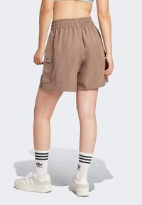 Brown cargo shorts with an elastic waistband, featuring side pockets and a relaxed fit. Worn with white sneakers and striped socks.