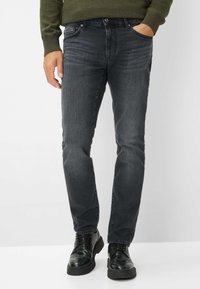 Jeans en denim gris foncé avec une coupe ajustée, dotés de cinq poches, d'une fermeture à bouton et d'une décoloration subtile. Associés à des chaussures brogues noires.