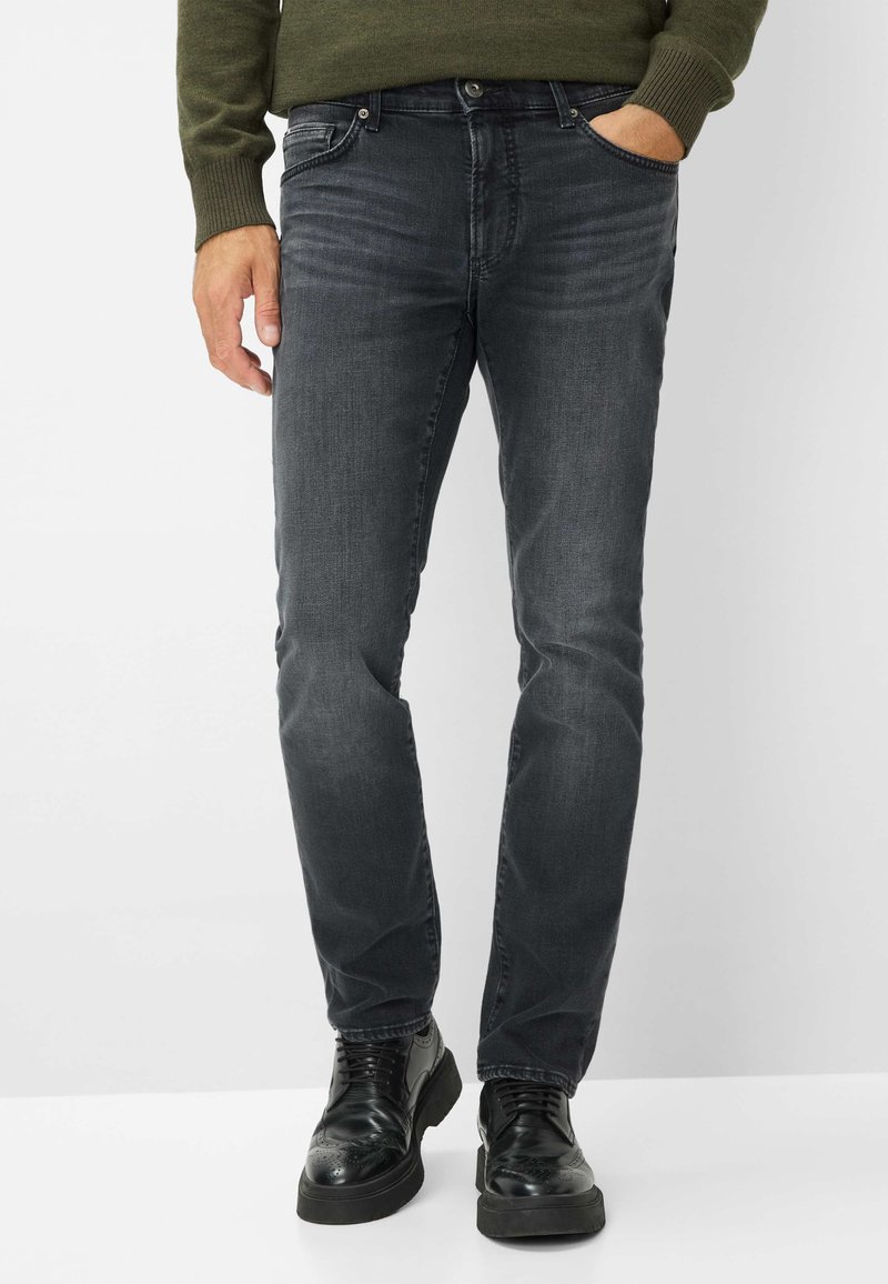 Jeans en denim gris foncé avec une coupe ajustée, dotés de cinq poches, d'une fermeture à bouton et d'une décoloration subtile. Associés à des chaussures brogues noires.