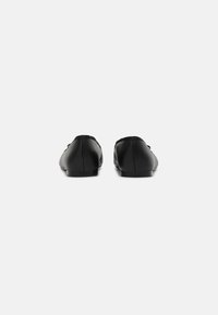 Mocasines de cuero negro con un acabado suave, punta redondeada y sutiles acentos elásticos en los laterales para mayor flexibilidad.