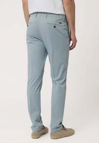 Lichtblauwe broek met een gladde textuur, met details op de achterzak en een licht taps toelopende pijp. G gedragen met grijze instap schoenen.