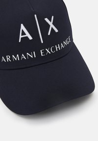 Navy blue cap made of polyester with a curved brim. Features embroidered white "A/X" logo and "ARMANI EXCHANGE" text on the front.