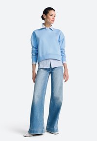 Hele sinine puuvillane dressipluus kantuna valge ja sinise triibulise särgi peal, mille juures on laia lõikega kulunud sinised teksad ja hõbedased võrgust jalanõud.