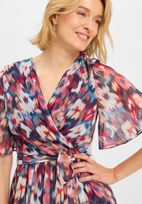 Multikleurige wikkeljurk van lichtgewicht, vloeiende stof. Heeft korte, fladderende mouwen en een getailleerde taille, met een kleurrijk abstract patroon.