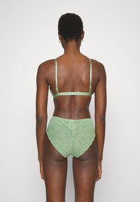 Conjunto de lingerie verde em renda, apresentando um sutiã de cetim com alças ajustáveis e uma calcinha de cintura alta que exibe padrões florais intrincados.