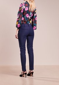 Bluzka w kwiatowy wzór z rękawami do połowy przedramienia i wysokim dekoltem, zestawiona z dopasowanymi granatowymi spodniami i czarnymi butami na wysokim obcasie.