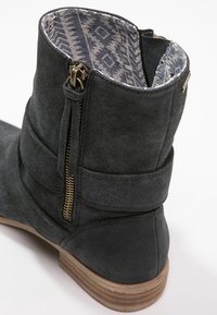 Šedá semišová kotníková bota se zipem, strukturovaným tvarem, dekoračními pásky a vzorovanou látkovou vycpávkou uvnitř. Dřevěný podpatek jako akcent.