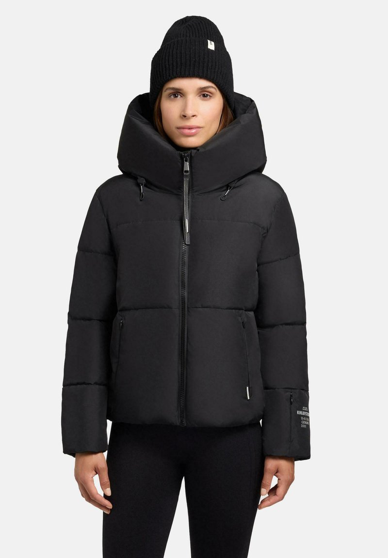 Sort polstret jakke med høj krave og lynlås, med sidelommer og diskret branding på ærmet. Blød tekstur og isoleret design.