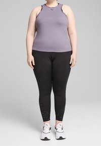 Svetle fialové sportovní tílko s černými akcenty v kombinaci s černými legínami s bočním vzorem. Bílé tenisky tvoří celkový vzhled.