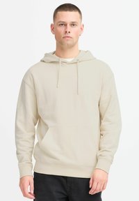 Felpa beige con tasca a marsupio frontale, cappuccio regolabile con lacci e polsini a coste. Realizzata in materiale morbido con una texture liscia.