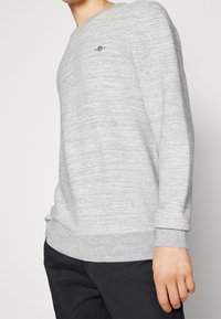 Sweatshirt gris clair avec un design texturé en côtes. Présente un col rond et des poignets ; petit logo brodé sur la poitrine.