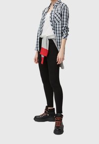 Leggings neri, t-shirt bianca e camicia a quadri blu, con un maglione grigio legato in vita. Stivaletti neri robusti con dettagli rossi.