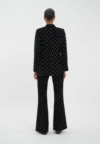 Costume en velours noir avec des motifs d'étoiles dorées ; veste ajustée et pantalons évasés, présentant une texture lisse et un léger éclat.