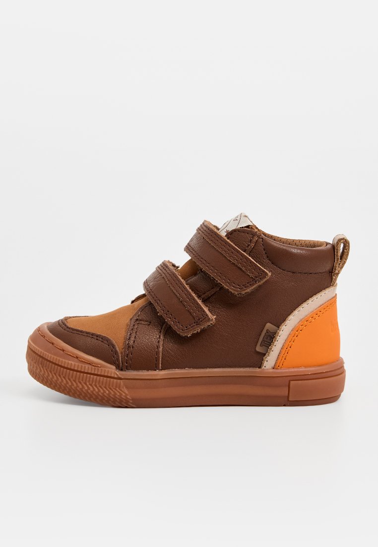 Bruine leren hoge schoen met oranje accenten, voorzien van twee klittenbandstrappen, rubberen zool en een contrasterend beige paneel aan de zijkant.