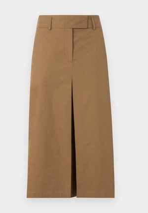 Žena má na sebe čiernu krátku bundu, čierny rolák, hnedú midi sukňu s predným rozparkom, čierne podpatky a drží čiernu kabelku, stojí.