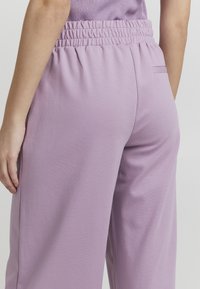 Liliowe spodnie z elastycznym paskiem w luźnym kroju. Gładka struktura, z boczną kieszenią i subtelnym haftem na pasku.