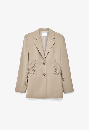 Beige tailored blazer with notch lapels, two front buttons, side lace-up detailing, and long sleeves, laid flat on a white background.