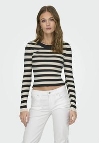 Maglia a maniche lunghe a righe nere e crema, con taglio cropped, abbinata a pantaloni bianchi. Tessuto liscio, scollatura rotonda e design aderente.