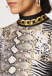 Printed garment features snake and animal patterns in gold, black, and white. A thick gold chain detail accents the black collar.