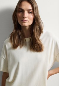 T-shirt oversize crema chiara in tessuto morbido con scollo a costine e maniche corte, caratterizzato da una vestibilità rilassata e una texture liscia.