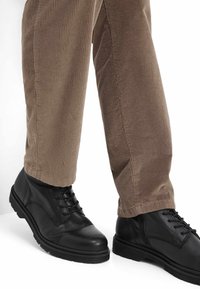 Zwarte leren veterschoenen met een ronde neus en een gestructureerde afwerking, gecombineerd met ribbelige bruine corduroy broek.