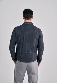 Pánská tmavě šedá džínová bunda s klopovým límcem, viditelným prošitím a nášivkou s logem na horní části zad. Outfit doplňují šedé kalhoty.