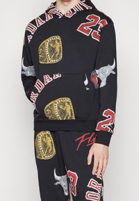 Sudadera con capucha de mezcla de algodón negro con grandes gráficos coloridos, incluyendo toros, aros y el número 23, con un bolsillo tipo canguro en la parte delantera.