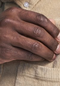 Main visible de couleur brune avec une texture et des caractéristiques de peau reposant sur un tissu en velours côtelé beige avec des côtes verticales et deux boutons au-dessus.