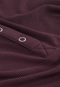 Bordeauxfarbenes geripptes Material mit einer Knopfleiste, die mit silbernen Beschlägen ausgestattet ist. Die Textur ist weich, mit diagonalen Rippungen und einem subtilen Glanz.