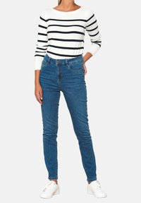 Slim-fit blue jeans with a high waist, paired with a long-sleeve white top featuring navy horizontal stripes; model wears white sneakers.