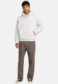 Grijze katoenen hoodie met een voorzak en een capuchon met trekkoord, gecombineerd met bruine broek en zwart-witte sneakers.