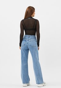 Sort gennemsigtig langærmet top med høj hals, parret med højttaljede blå denim vide jeans. Hvide sneakers fuldender outfittet.