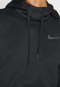 Gros plan sur une personne portant un hoodie noir Nike avec des cordons de serrage et un logo swoosh Nike gris sur la poitrine.