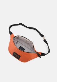 Orange Bauchtasche aus glattem Material mit einem verstellbaren schwarzen Gurt. Verfügt über einen Reißverschluss und eine Innentasche mit Branding im Inneren.