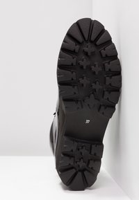 Chaussures noires avec une semelle texturée robuste, présentant des crampons profonds et une étiquette de taille "37" imprimée en dessous.