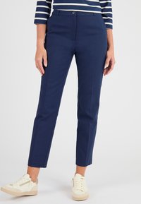 Pantaloni navy su misura con una vestibilità slim, dotati di chiusura con bottone, tasche laterali e tessuto morbido; abbinati a sneakers crema.