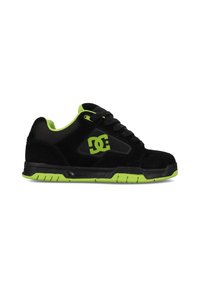 Zapatillas de ante negras con acentos verdes, que cuentan con un cuello acolchado, lados texturizados y suela de goma. Logo de DC mostrado en el lateral.