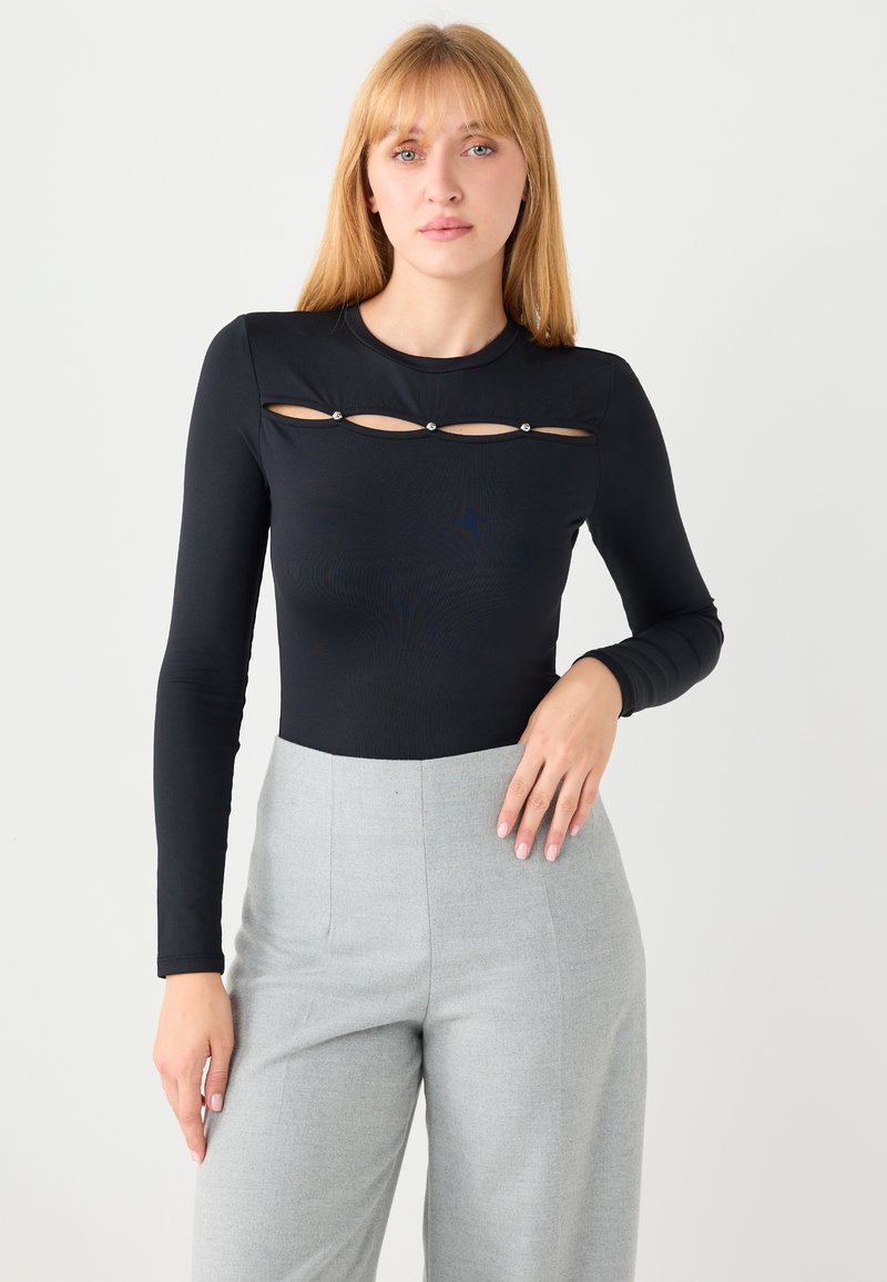 Schwarzer langärmliger Bodysuit mit Ausschnittdetail am Brustbereich, akzentuiert durch drei metallische Nieten. Glatter, dehnbarer Stoff. Kombiniert mit grauen Hosen.