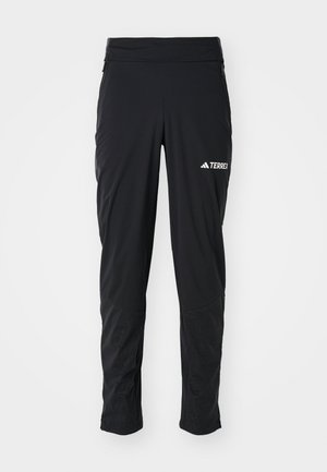 Musta ulkoiluhousut sileällä pinnalla, joissa on vetoketjulliset taskut, istuva vyötärö ja teksturoidut yksityiskohdat alhaalla. Koristeltu Terrex-logolla.