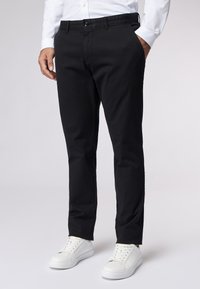 Schwarze Baumwollhosen mit schmaler Passform, ausgestattet mit Seitentaschen und einer glatten Textur. Getragen mit weißen Sneakern für den Kontrast.