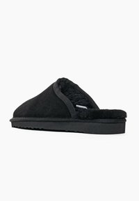 Musta nukka kengän kanssa tekoturkisvuori, avoin takaosa ja teksturoitu kumipohja. Yksinkertainen muoto, tasainen profiili, ei näkyvää metalliosaa.