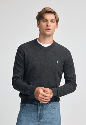 Dunkelgrauer V-Ausschnitt-Pullover aus weichem Strickstoff, mit langen Ärmeln und kleinem Logo auf der Brust, kombiniert mit hellblauen Jeans.