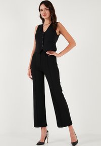 Black vest top with a v-neck and four buttons, paired with high-waisted black wide-leg trousers. Satin texture, sleek design, and tailored fit.