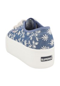 Modré džíny tenisky s bílou květinovou výšivkou, s kulatou špičkou, silnou bílou podrážkou a štítkem s nápisem "SUPERGA" na patě.