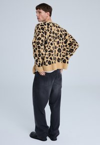 Maglione in maglia con stampa leopardata in tonalità beige e macchie nere, dal taglio loose fit, con polsini a coste, abbinato a jeans grigi scuri dal taglio rilassato e scarpe nere.
