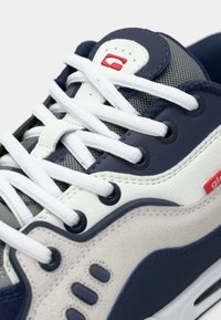 Adidași cu un superior din piele albastră închisă, șireturi albe, plasă gri și accente roșii. Au vârful rotunjit și talpa din cauciuc cu un model distinct.