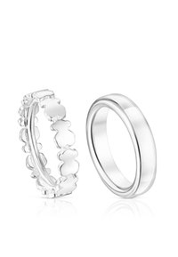 Dos anillos de plata uno al lado del otro, uno con una banda sólida y lisa y el otro con un patrón entrelazado de formas de osos de peluche.